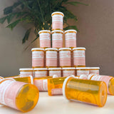 Each container displays similar branding with text emphasizing acrylic restoration. Several other containers are scattered at the base of the pyramid, all placed on a clean white surface. The background features a leafy green plant and neutral-colored walls, enhancing the minimal and organized presentation.