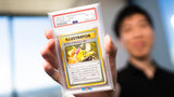 Person holding a PSA-graded 1998 Pikachu Illustrator Japanese Promo card, rated NM-MT 8, one of the rarest Pokémon cards in existence.