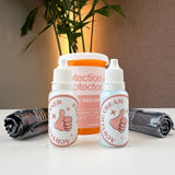 A display of cleaning products designed for maintaining acrylic cases. The kit includes two small bottles labeled "Acrylic Cleaner" and "Acrylic Cream," both with thumbs-up icons. Behind them, there is a larger orange container labeled "Protection + Protector Acrylic Restoration Kit.